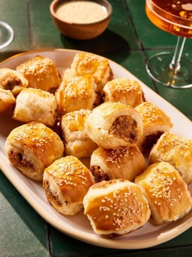 White platter with puff pastry sausage bites piled on top of each other all on green tiles.