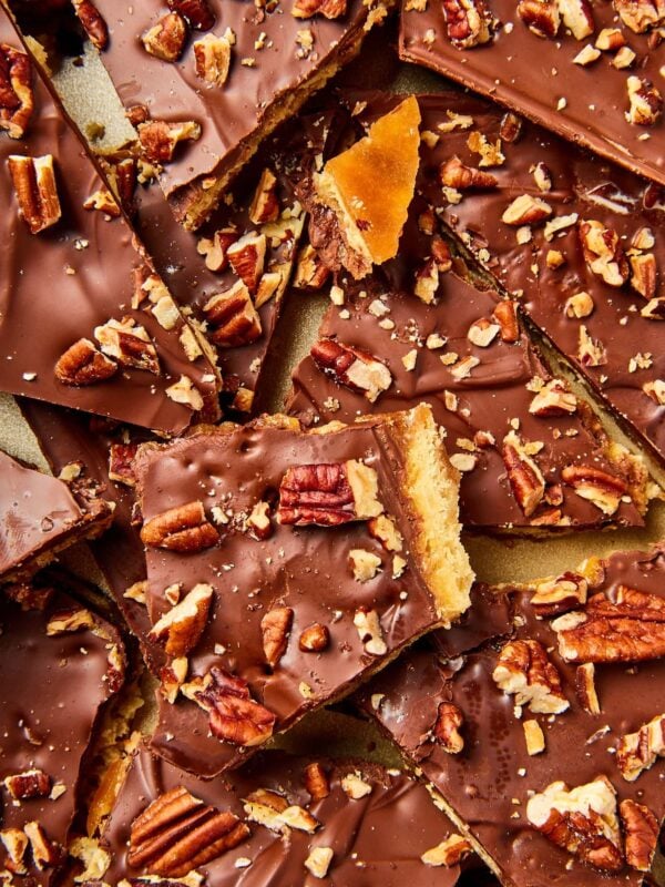 Piles of saltine toffee broken into pieces resting on top of each other in gold baking pan showing pecans and interior saltine texture.