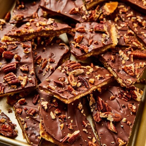 Piles of saltine toffee with chopped pecans sprinkled over the top resting together in gold baking pan.