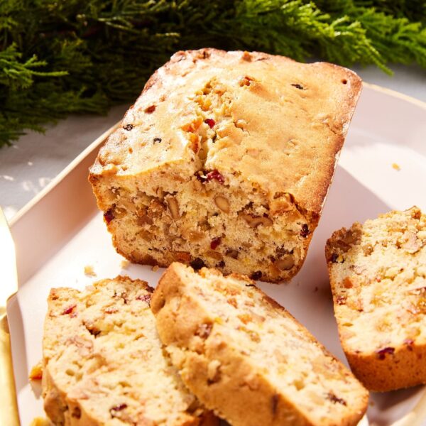 White serving platter filled with slices of white fruitcake with rest of loaf along with gold knife.