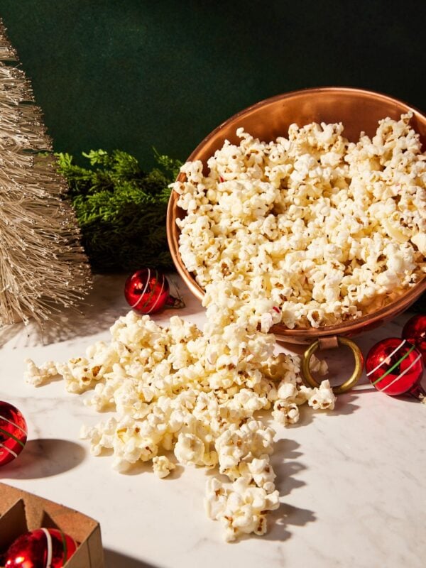 Copper bowl filled with white chocolate peppermint popcorn spilling out onto marble surface.