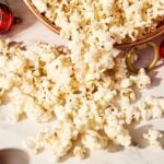White chocolate peppermint popcorn spilling out of a copper bowl onto white marble surface with pieces of crushed peppermint.