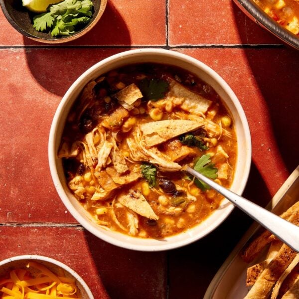 Bowl of chicken tortilla soup sitting on red tile surface filled topped with crispy tortilla strips.