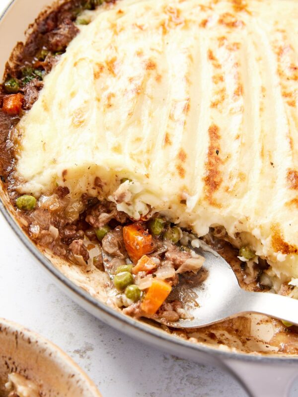 Spoon resting against side of pot filled with shepherd's pie mixture with spoon about to lift up some of the beef, corn, and peas.