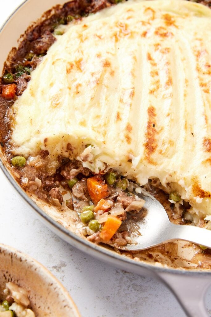 Spoon resting against side of pot filled with shepherd's pie mixture with spoon about to lift up some of the beef, corn, and peas.