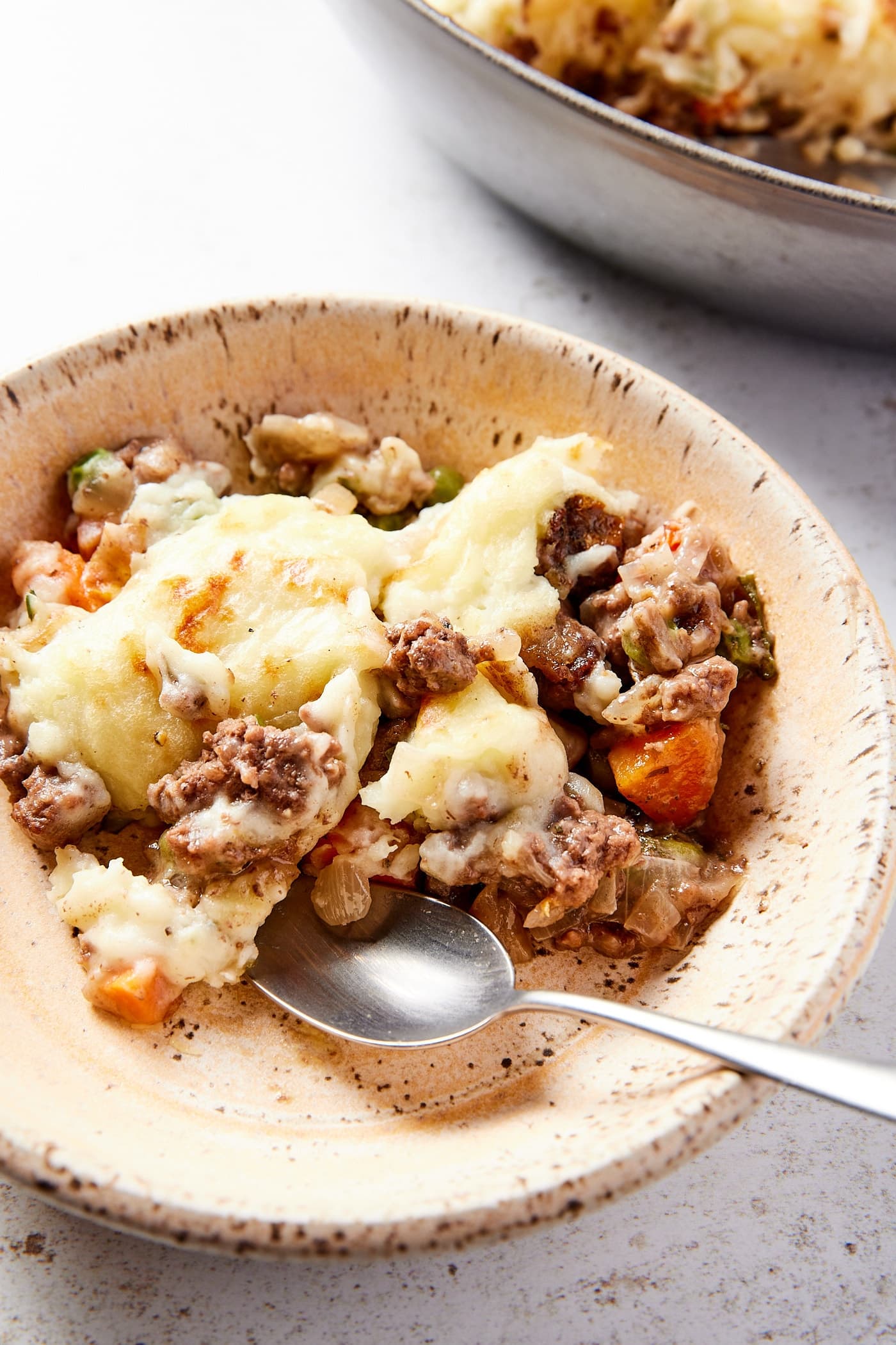 Stoneware bowl filled with serving of shepherd's pie with spoon resting against the side of bowl.
