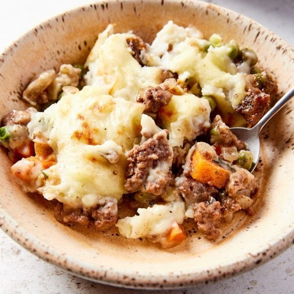 Stoneware bowl with single serving of shepherd's pie with mashed potatoes and beef and carrots with spoon scooping up a serving.