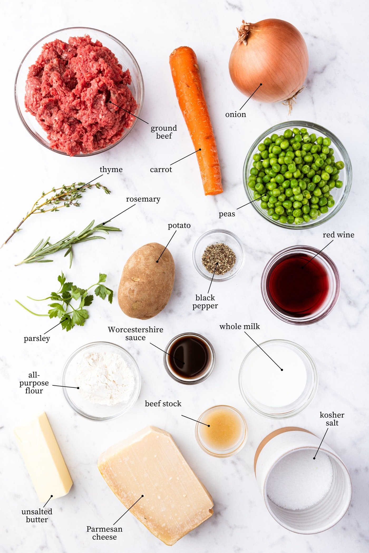 White marble surface filled with all ingredients needed to prepare shepherd's pie including beef, red wine, carrots, peas, potatoes, spices, and more.
