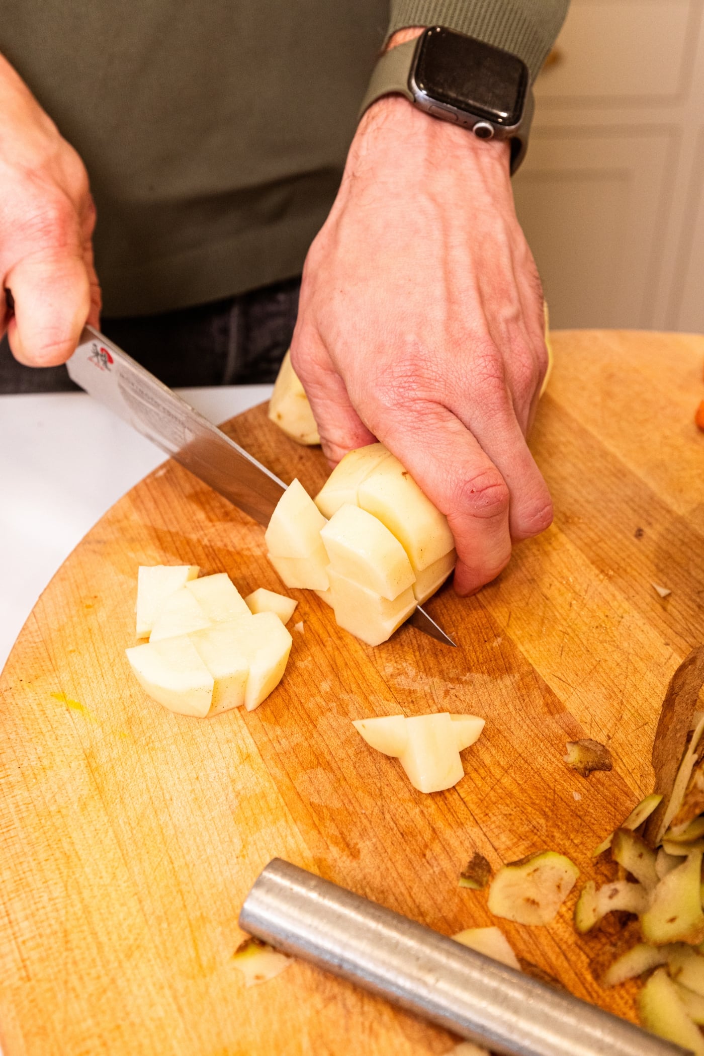 Two hands slicing potatoes on wooden cutting board.