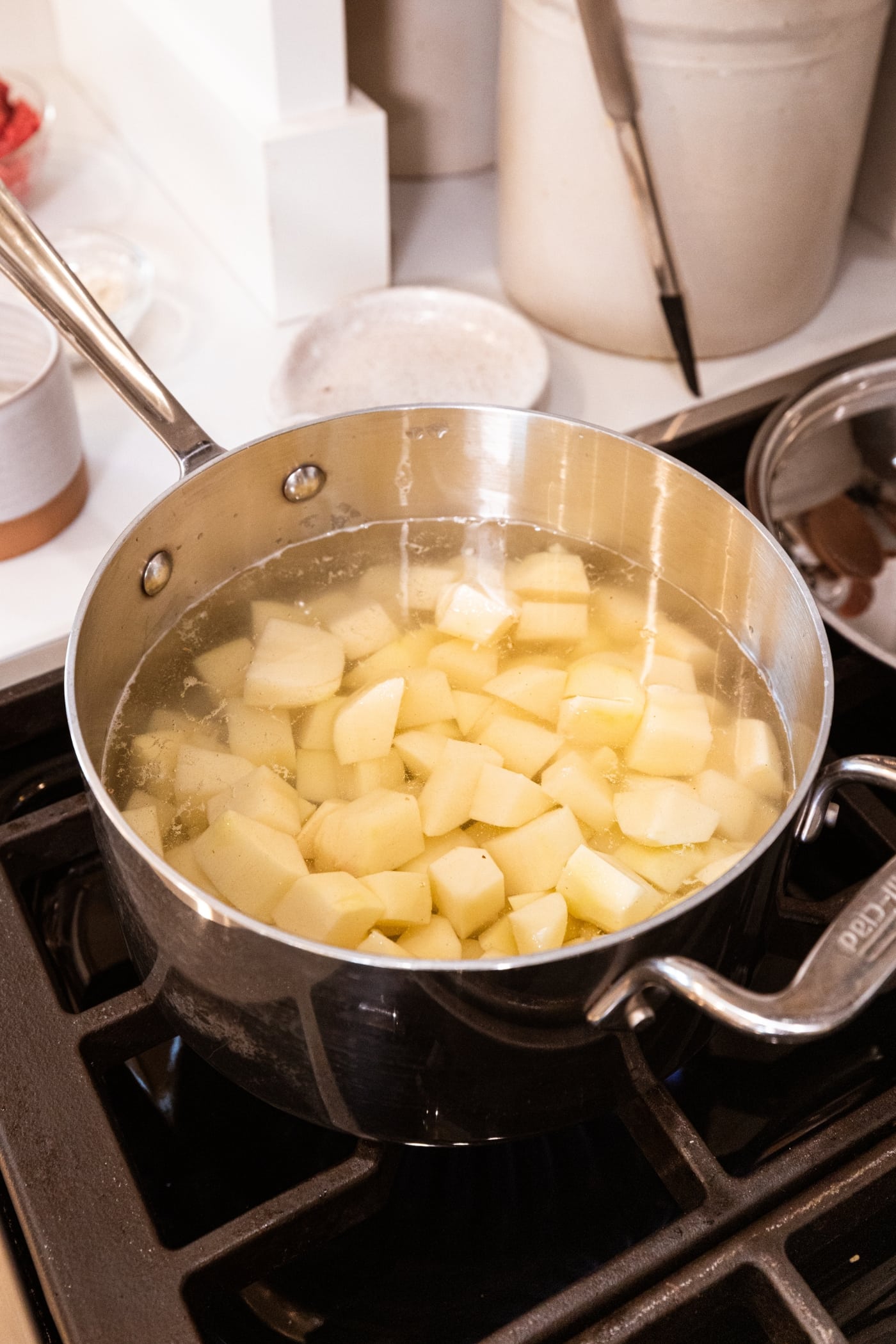Metal pot filled with slices of potato in water cooking on the stovetop.