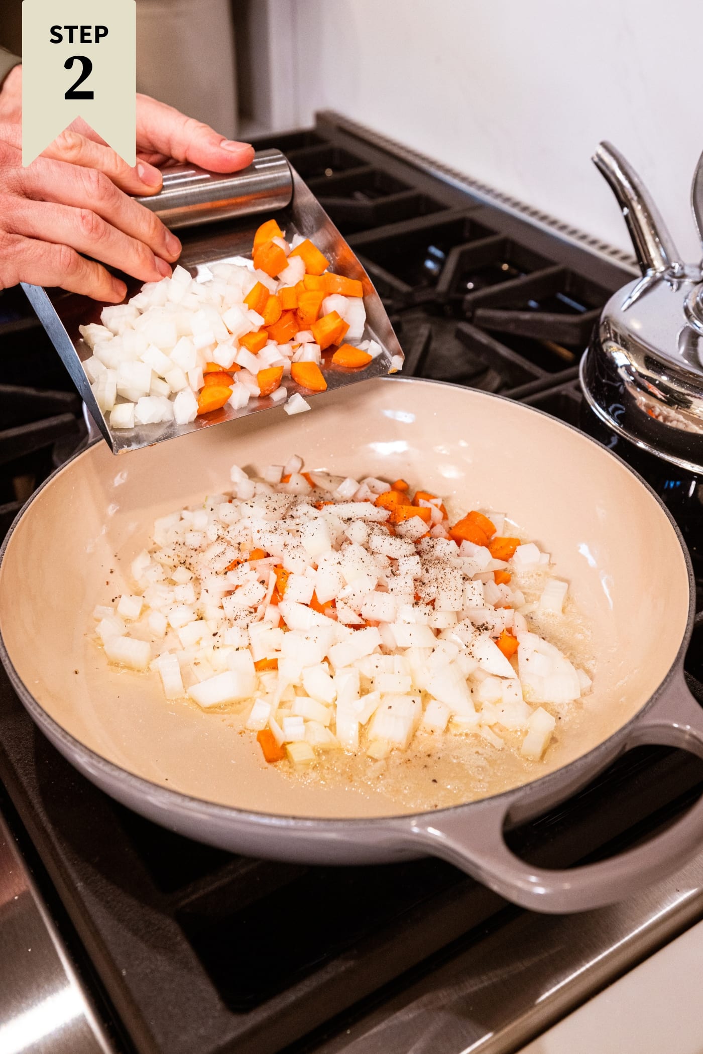 Hand about to push mixture of diced onion and carrot into a large pot on the stovetop.