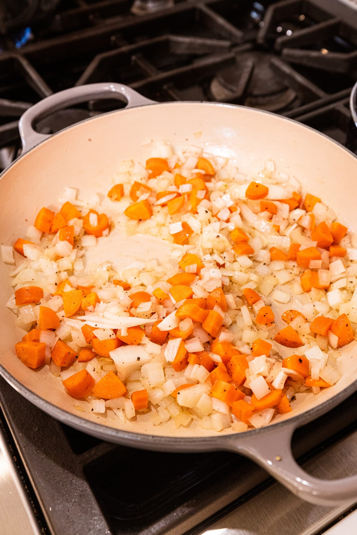 Large pot on stovetop with cooking pieces of diced carrots and onions after browning for a bit.