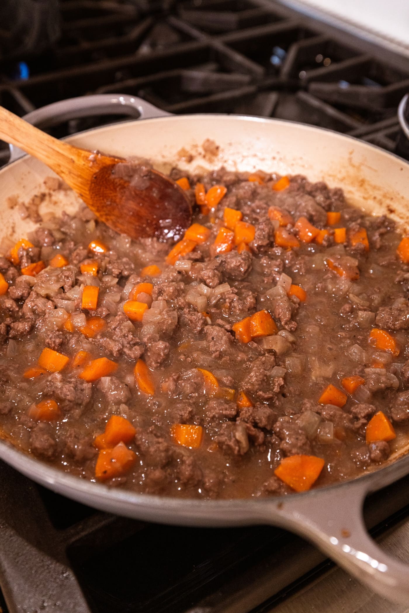 Wooden spoon stirring together mixture for base of shepherd's pie in a large pot on the stovetop.