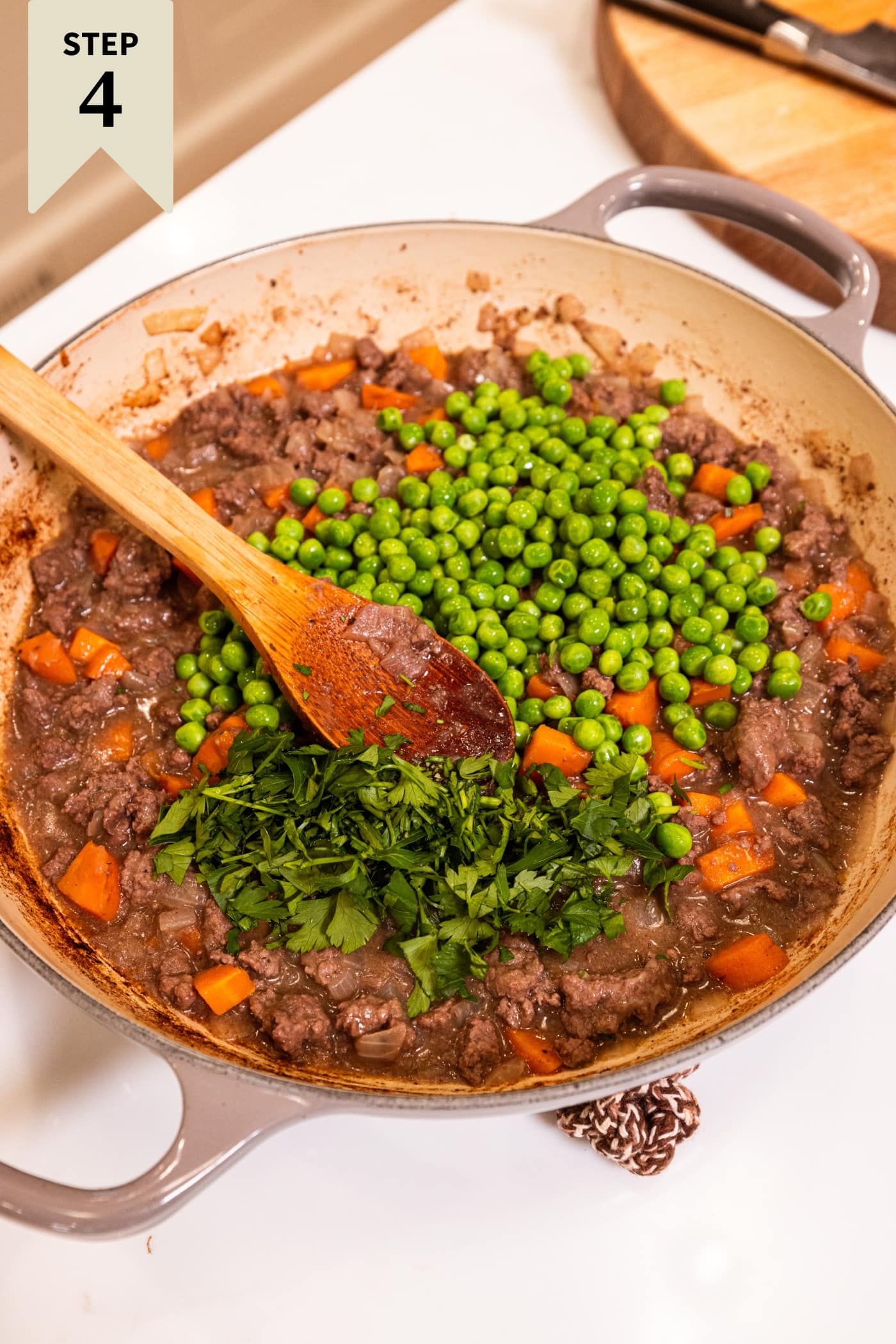 Wooden spoon resting against side of large pot right after herbs and frozen and thawed peas were added.