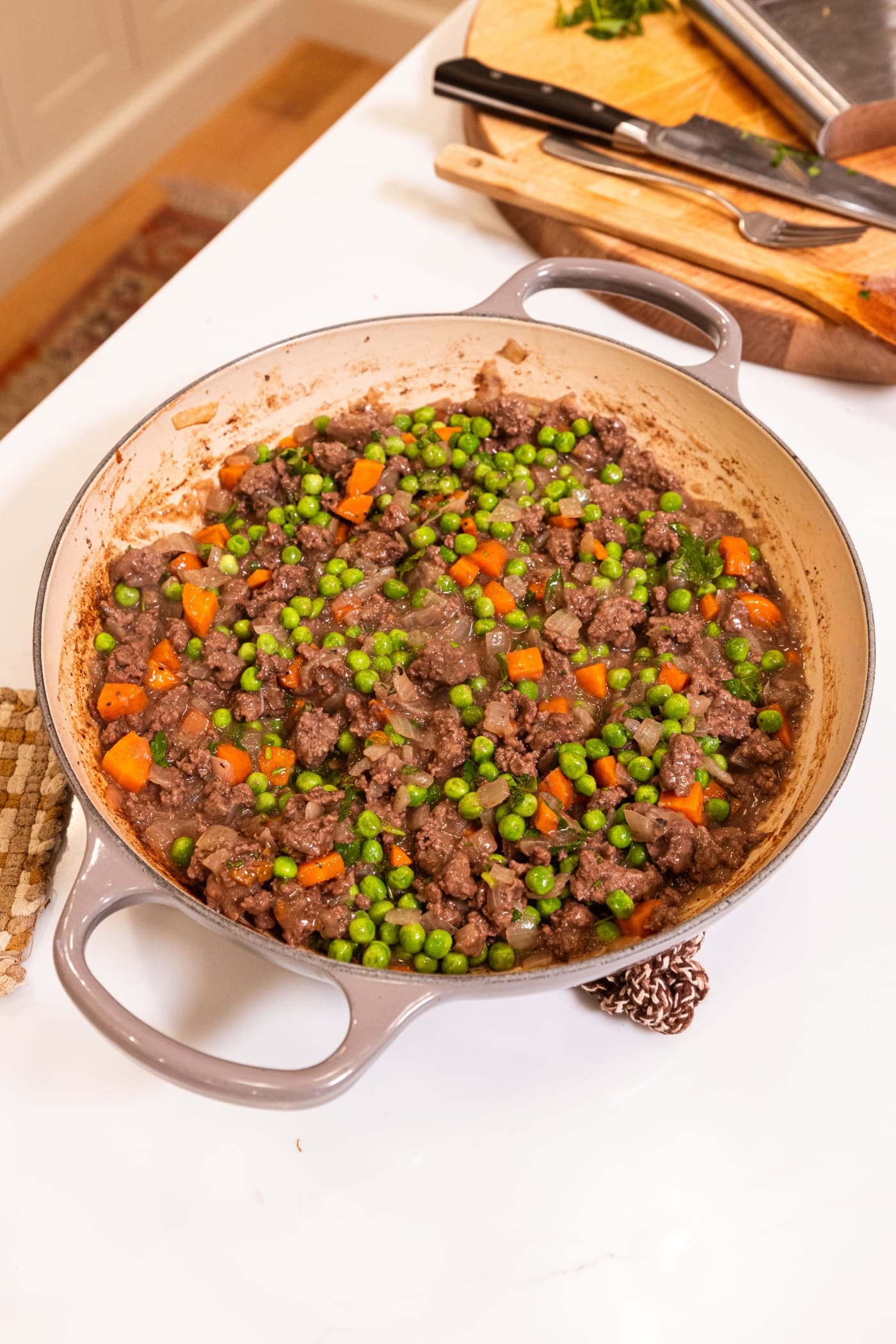 Peas mixed into a beef and carrot mixture in large pot on white surface to form shepherd's pie.