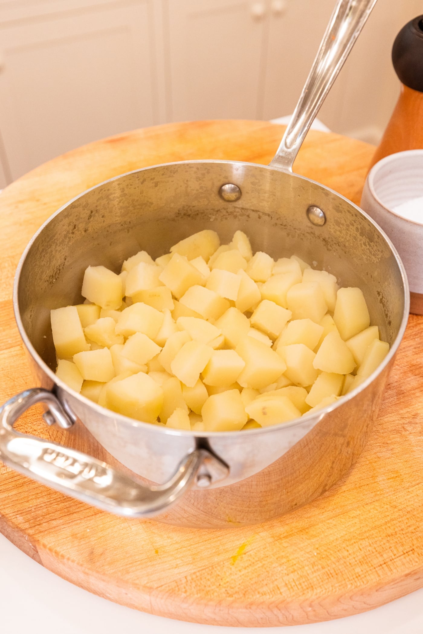 Cooked diced potatoes in large pot resting on wooden surface.