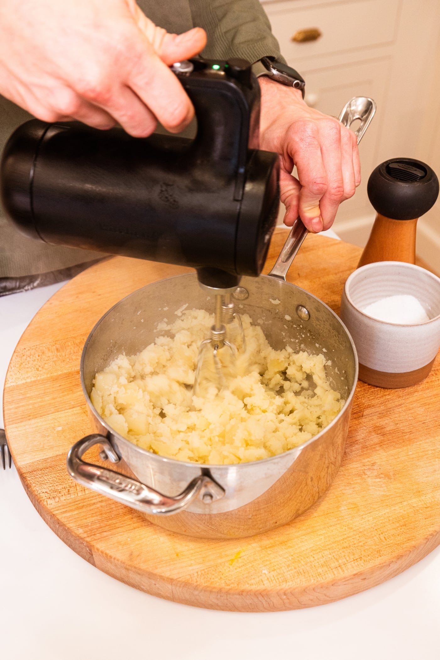 Hand holding mixer mixing potatoes together in metal pot to form mashed potatoes.
