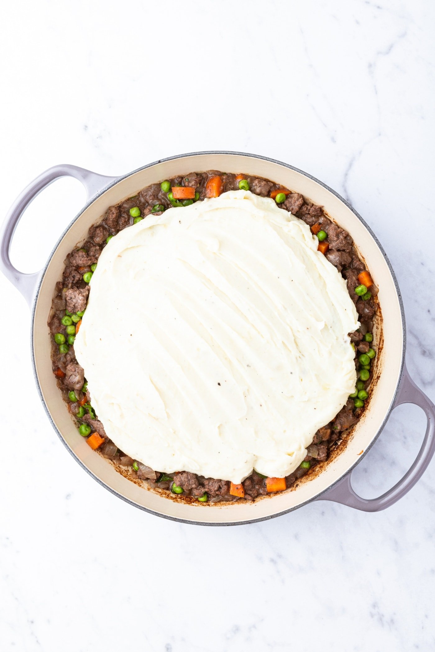 Large pot of shepherd's pie with mashed potatoes spooned on top right before going into the oven to warm everything through.