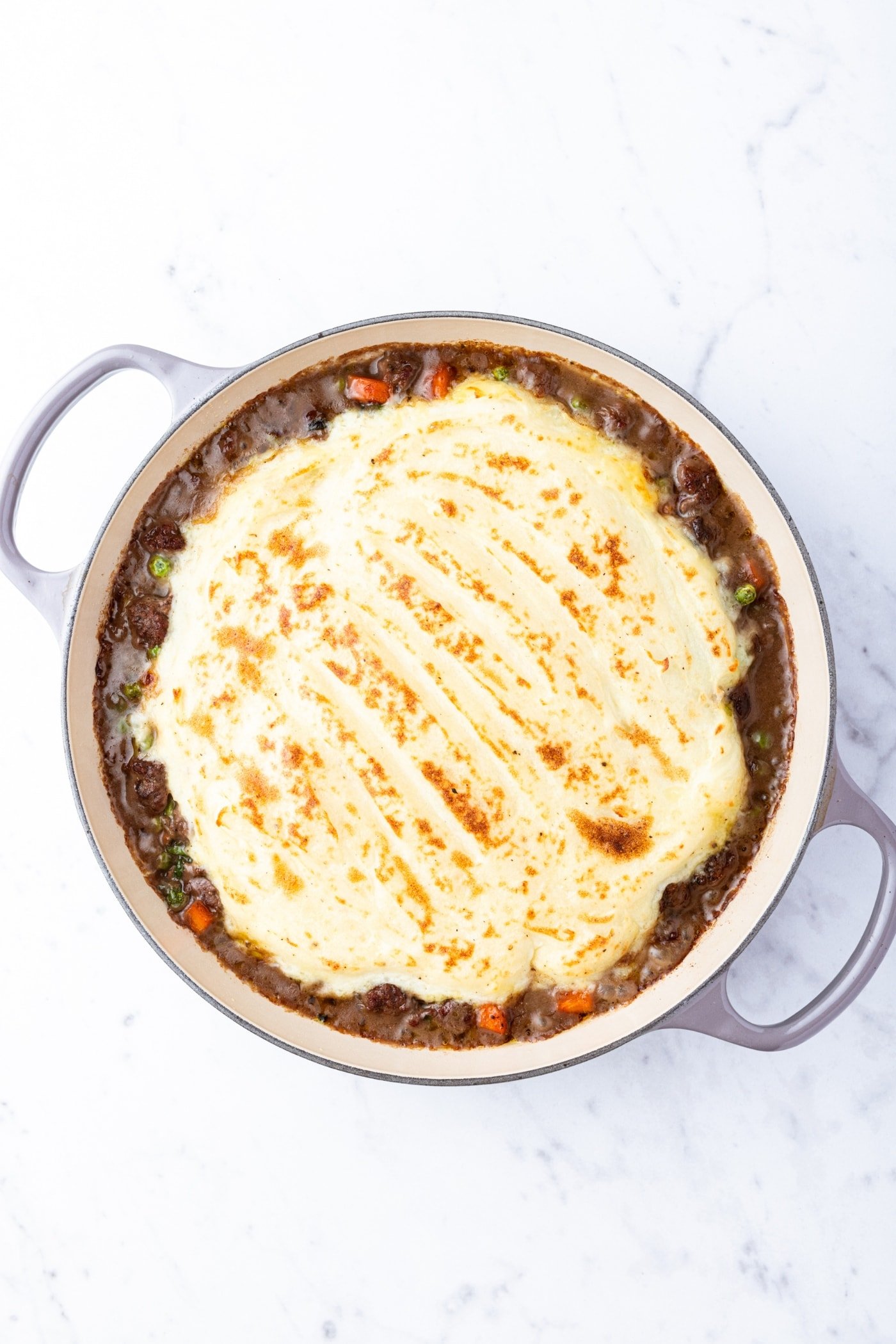 Large pot filled with shepherd's pie mixture with mashed potatoes on top right after browning in the oven.