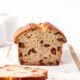 Loaf of chocolate chip banana bread resting on a wooden cutting board with slices resting in front all with white background.