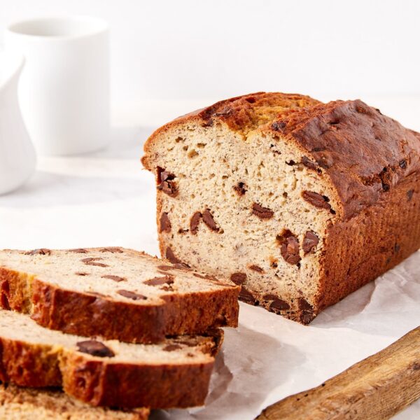 Loaf of chocolate chip banana bread on a wooden cutting board with slices cut.