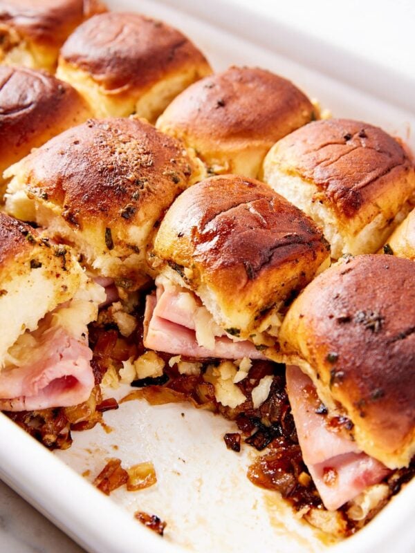 White baking dish filled with ham and onion jam sliders with a few sandwiches missing showing ham and cheese inside sandwiches.