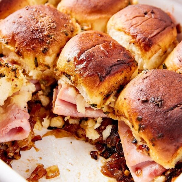 White baking dish with ham and onion jam sliders with a few sandwiches missing showing interior texture with ham and cheese.