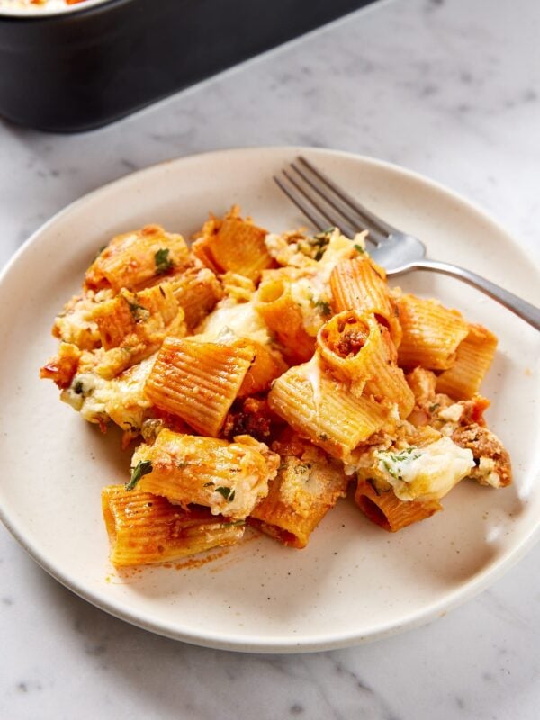 White plate with serving of lasagna casserole scooped on top with fork in the background.