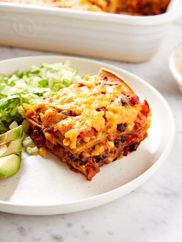 White plate with square piece of loaded taco squares casserole with pile of lettuce and avocado to the side.
