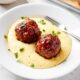 White plate filled with Parmesan polenta with meatloaf meatballs with ketchup sauce on top.