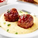 White plate filled with Parmesan polenta topped with two ketchup-covered meatloaf meatballs.