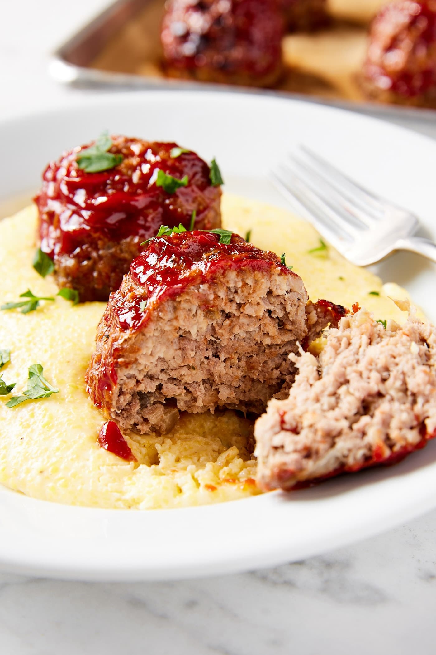 Meatloaf meatball sliced in half showing interior texture with Parmesan polenta underneath all on white plate.