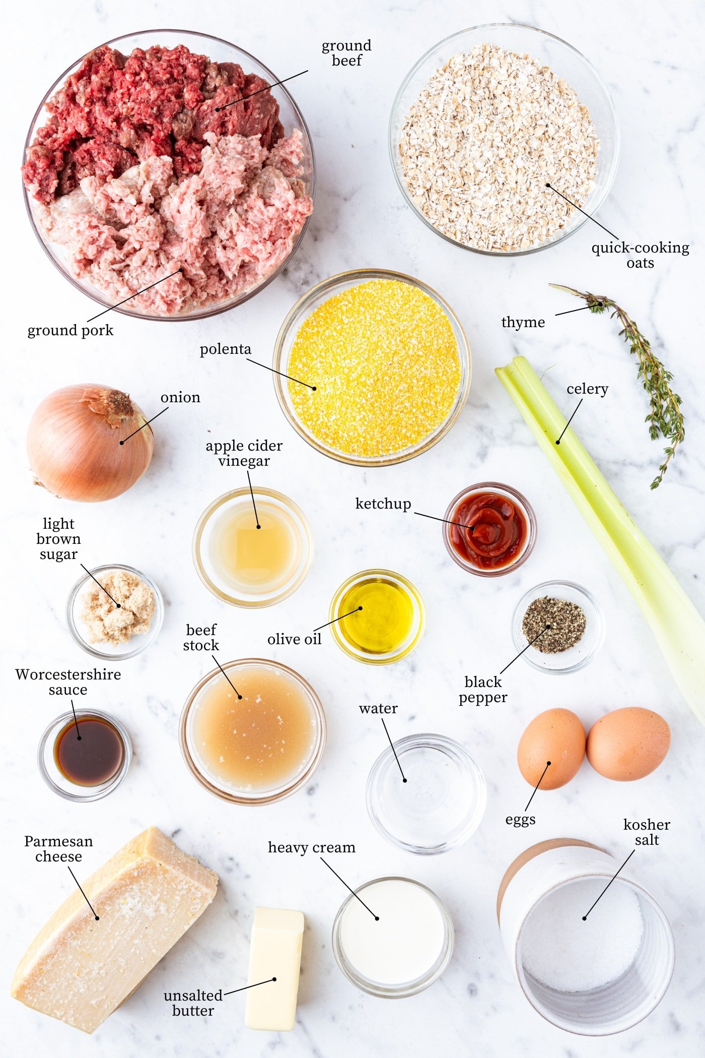 White marble surface filled with all ingredients needed to make meatloaf meatballs including meat, spices, polenta, brown sugar, Parmesan cheese, and more.
