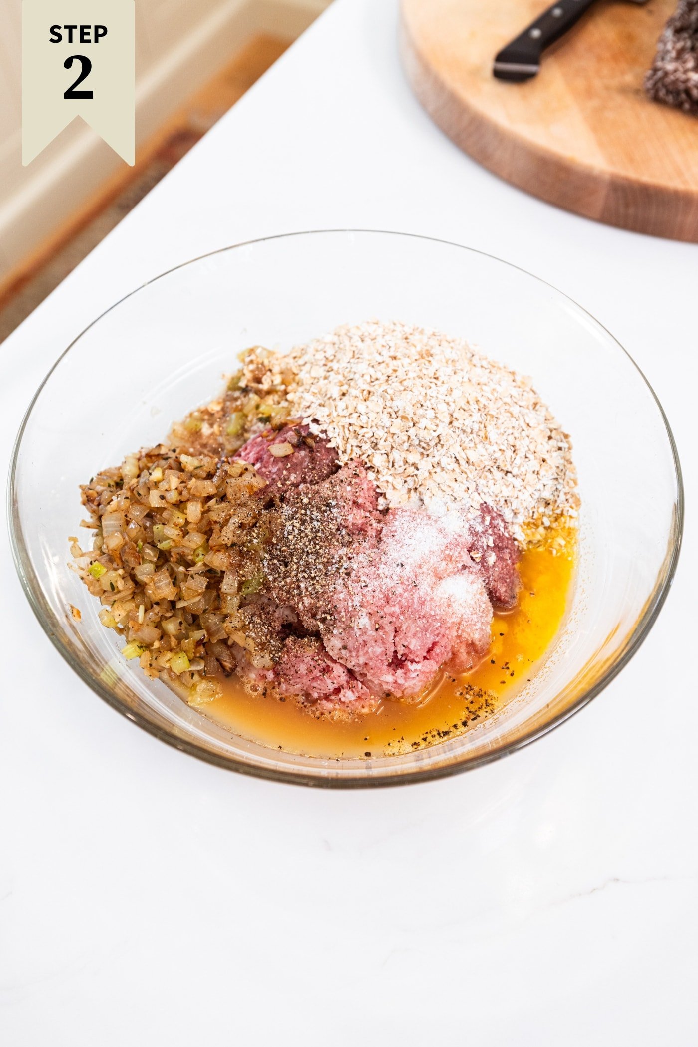 Glass bowl filled with all ingredients needed to form the base of a meatloaf meatball mixture.