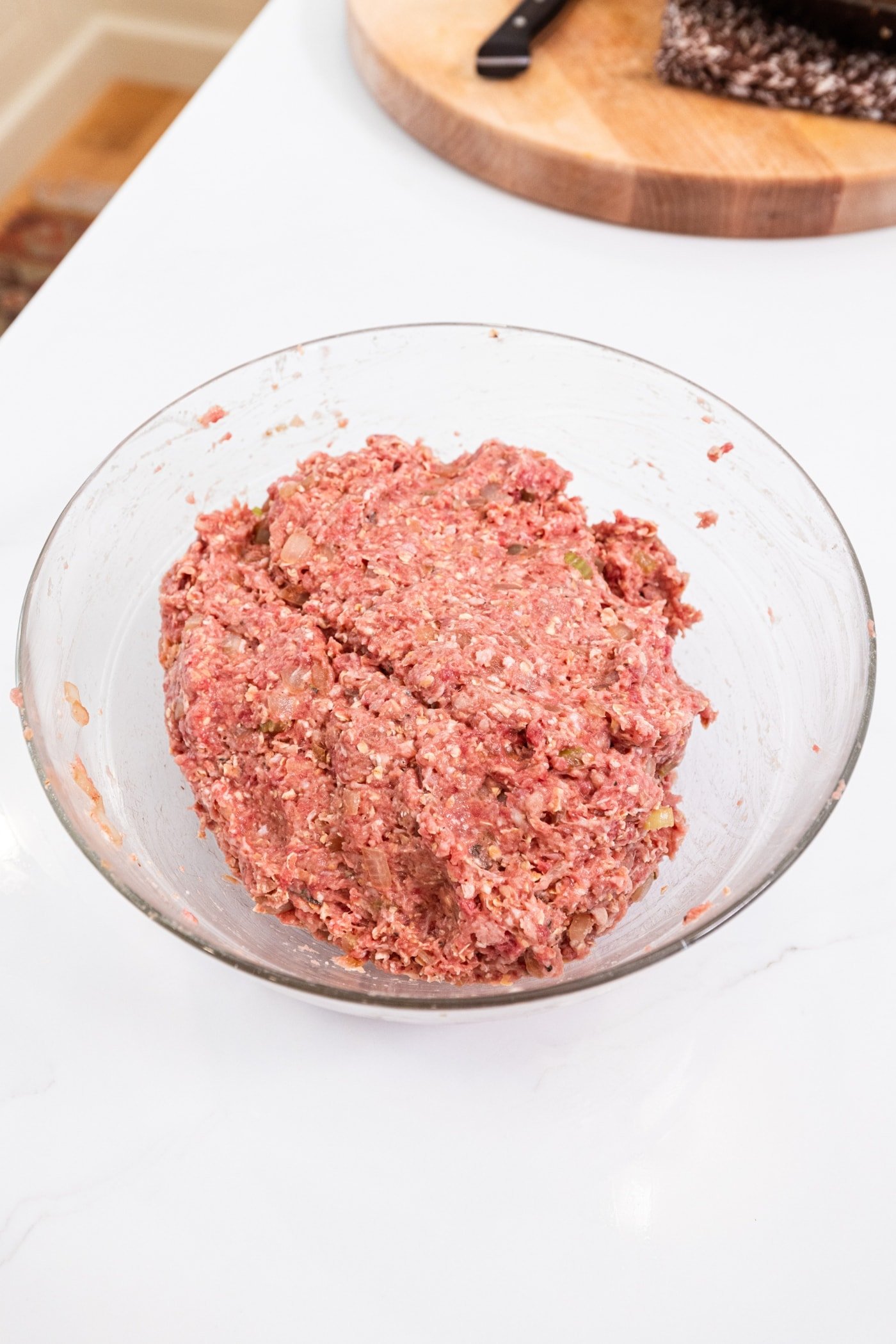 Glass bowl with mixture of beef and pork to form meatloaf meatballs all on white surface.