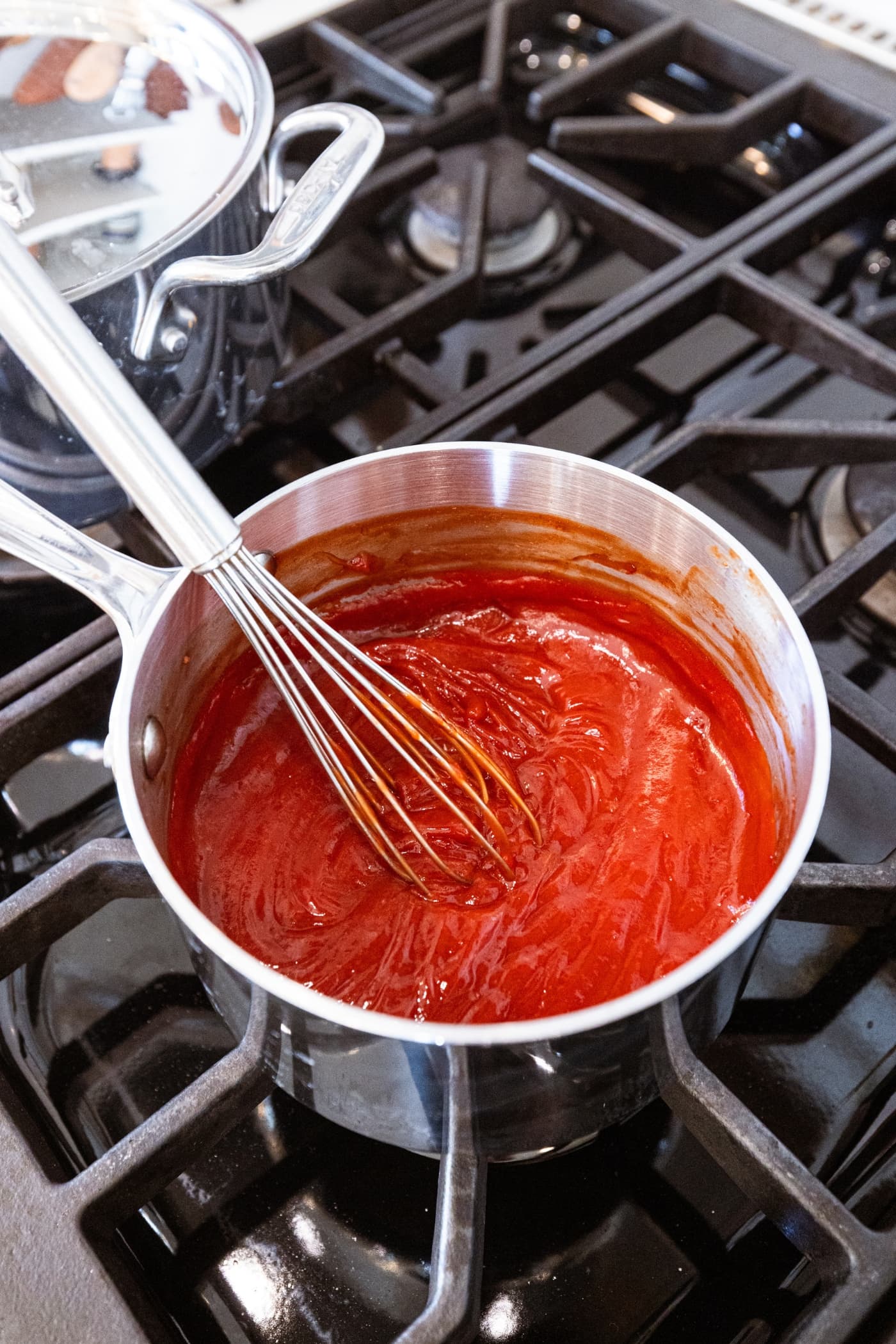 Metal saucepan filled with ketchup mixture used to cover meatloaf meatballs after cooking on the heat.