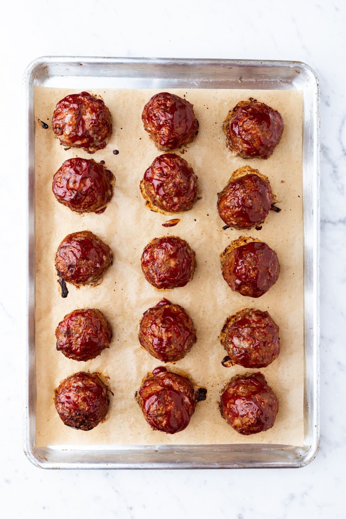 Meatloaf meatballs with ketchup mixture spread on top on a parchment-lined baking sheet right after coming out of the oven.