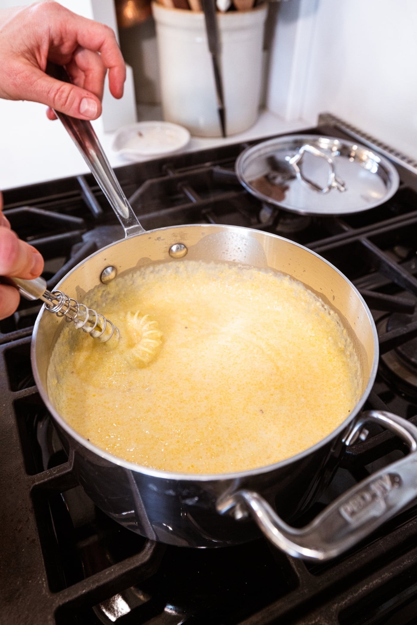 Creamy polenta mixture with whisk mixing everything together on a metal saucepan.