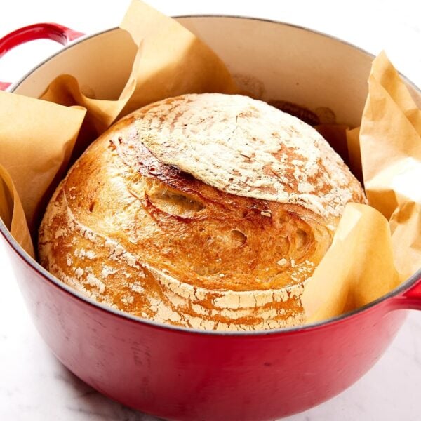 Red Dutch oven filled with baked golden brown overnight sourdough bread on white surface.