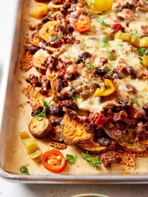 Sheet pan filled with layers of sweet potato chili nachos with pickled peppers, cilantro, and cheese sprinkled on top.
