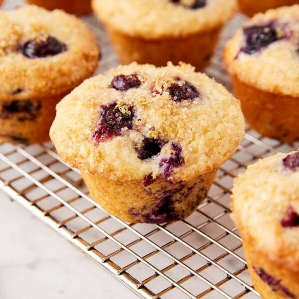 Wire cooling rack filled with baked blueberry muffins with lemon zest and turbinado sugar topping.