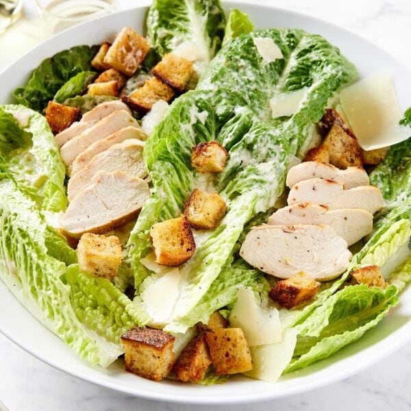 White bowl filled with chicken Caesar salad with homemade croutons and Parmesan cheese sprinkled on top.