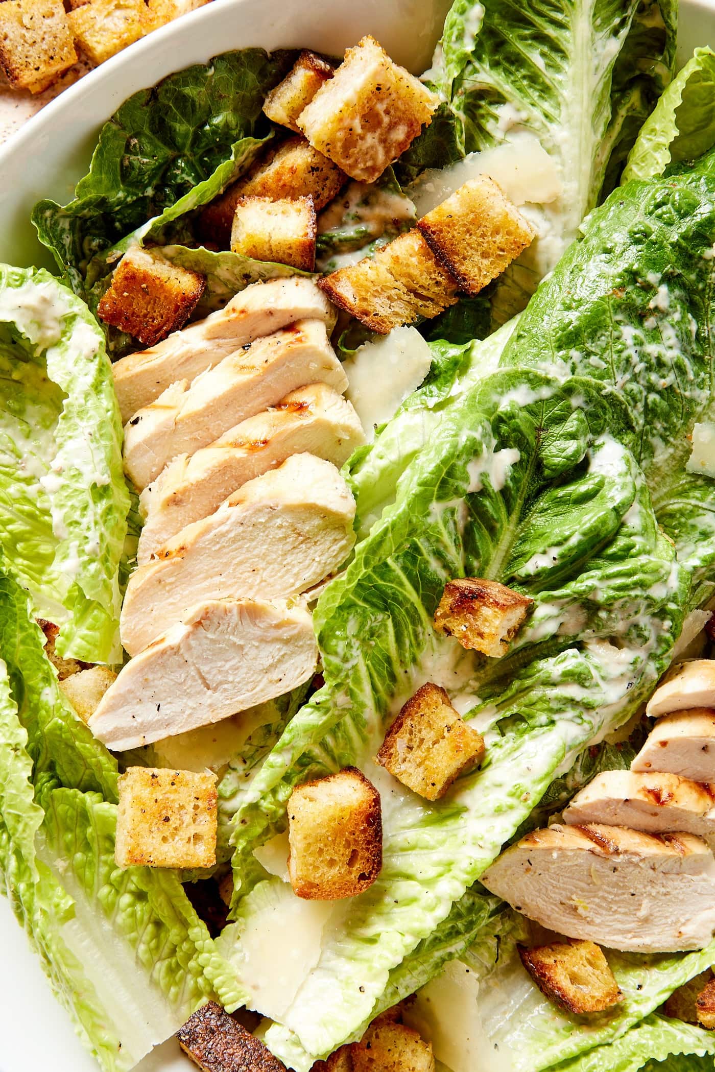 Large bowl filled with chicken Caesar salad with large pieces of romaine lettuce sprinkled with homemade croutons on top.