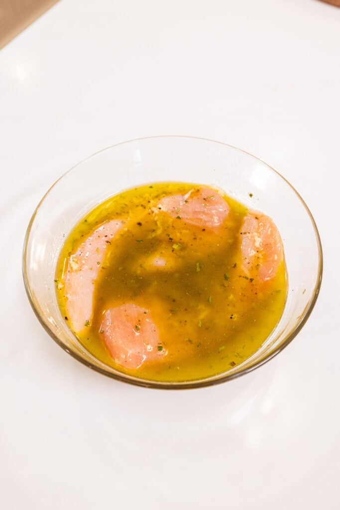 Glass bowl with raw chicken breast sitting in marinade marinating before being cooked.