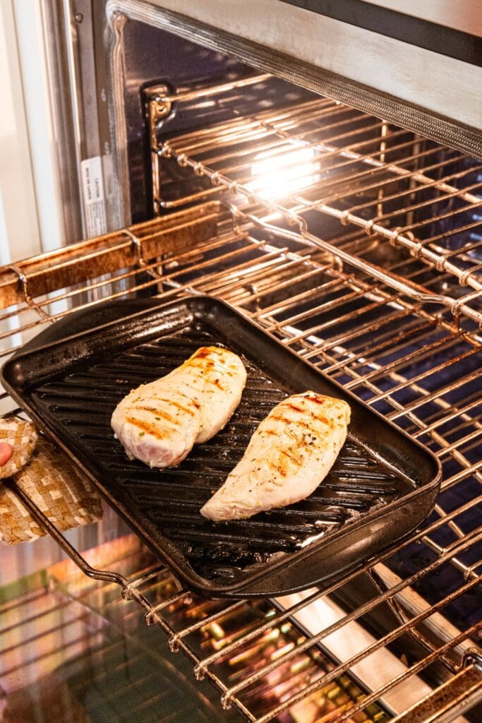 Grill pan with two chicken breasts resting on top going into a wall oven to finish baking.