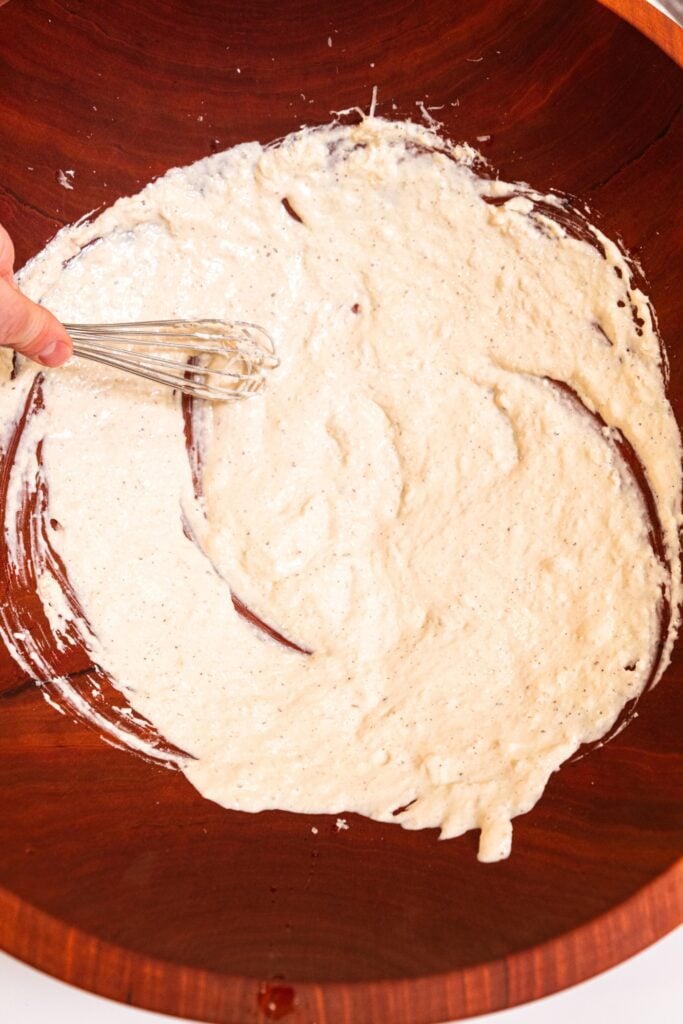 Homemade Caesar dressing being mixed with wire whisk in large wooden bowl before the lettuce is added.