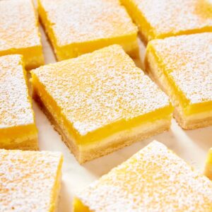 Lemon cheesecake bars resting on a white parchment surface dusted with powdered sugar showing each layer of the bar.