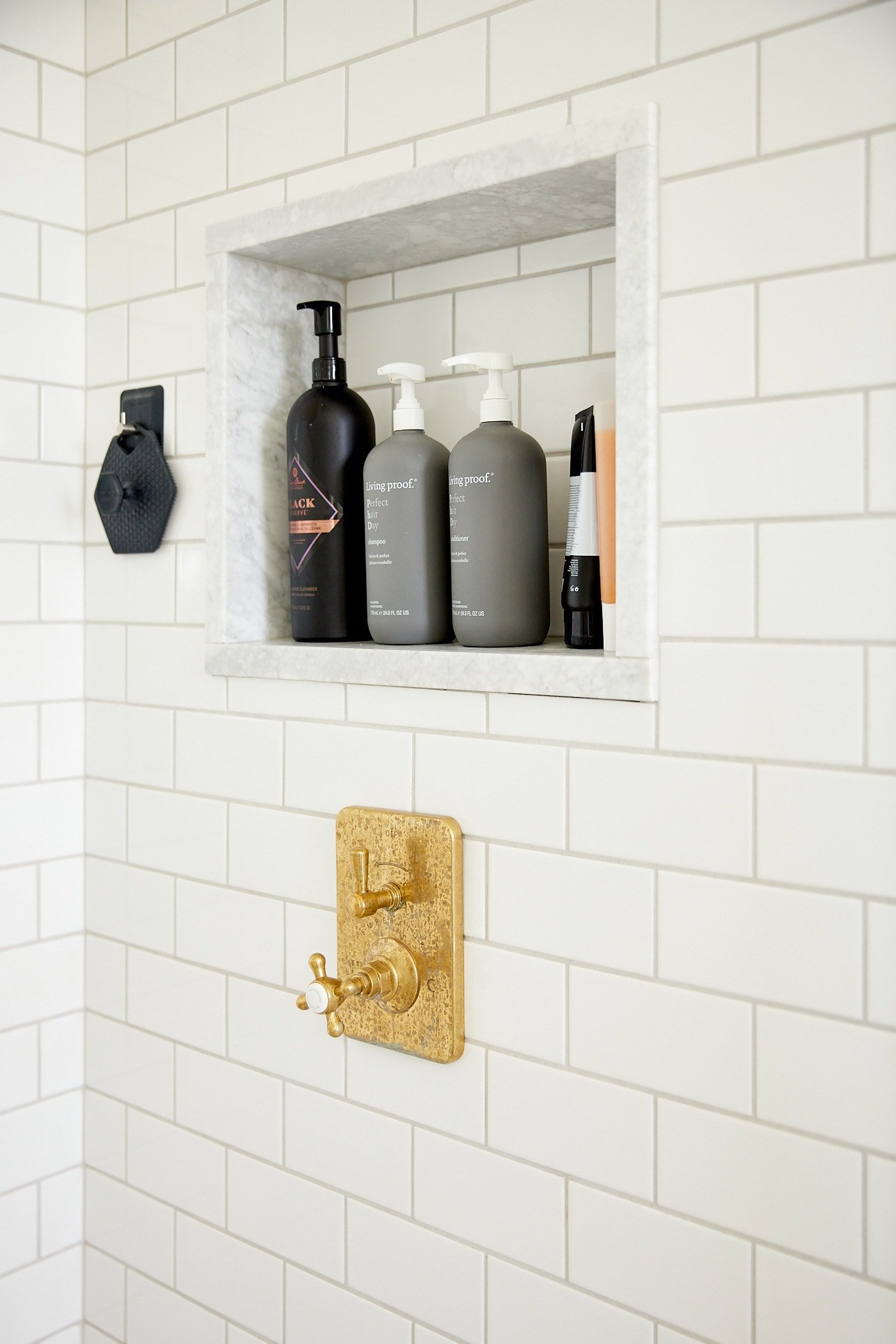 Subway tile all over a shower with shelf made from pieces of marble with unlacquered brass temperature control for shower.