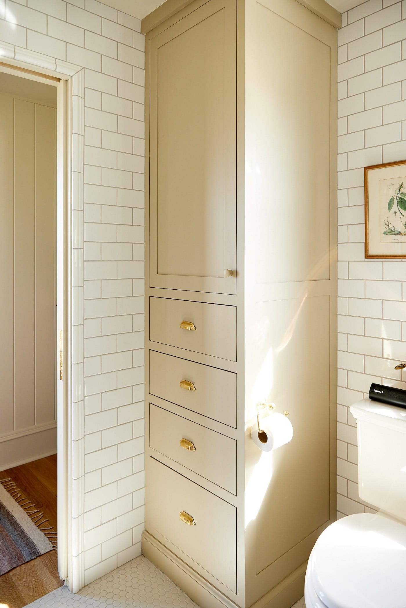 Small floor to ceiling cabinet hidden beside a toilet with tile on all of the walls.