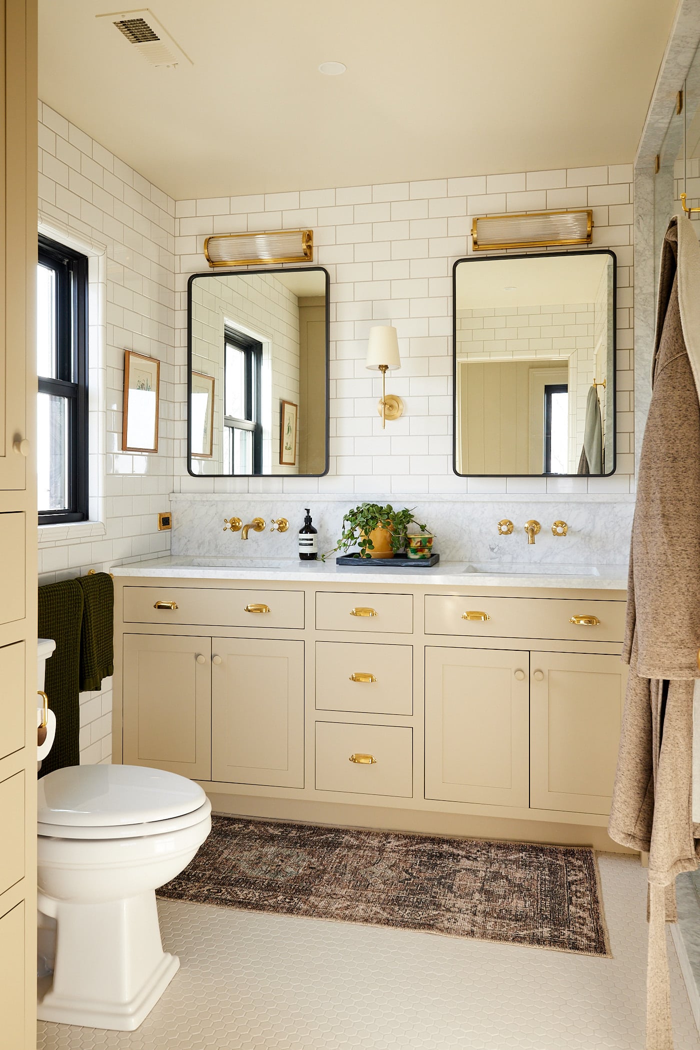 Bathroom with khaki colored cabinets and two mirrors with sinks with a toilet visible to the side.